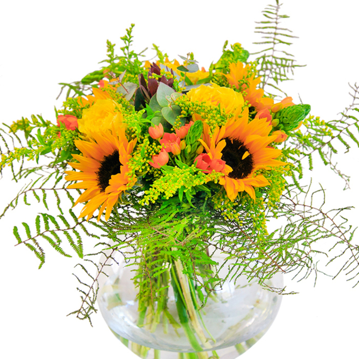 Offering a first impression reminiscent of a bright morning at the edges of Grove Park, this exuberant sunflower and rose arrangement brims with sun-kissed energy and local artistry. Towering sunflowers anchor the bouquet, their bold yellow petals radiating around dark, inviting centers-a cheerful homage to strolls through the community's verdant parks. Between them, golden yellow garden roses open layer upon layer, their tightly wound petals conjuring memories of visits to neighbourhood flower stalls. Deep crimson hypericum berries add dashes of lively colour, their luminosity contrasting vivid greens and evoking the vibrant side streets of Grove Park. Punctuating the composition are clouds of wispy fern fronds and frothy floral filler, filled with movement like summer wind in Chiswick's tree-lined avenues. Eucalyptus leaves in muted blue-green peek between, lending a gentle, herbal scent that lingers like the air after fresh rainfall. Supported by a crystal-clear, round glass vase, the sturdy stems and shimmering water are on display-celebrating natural beauty and honest craftsmanship from Grove Park Florist. Ideal for commemorating special milestones or simply to add joy to a living space, this bouquet honours the local essence and the uplifting artistry of a skilled floral designer rooted in Grove Park.